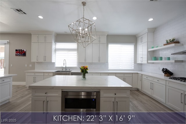 kitchen with light wood-type flooring, stainless steel microwave, a sink, and backsplash