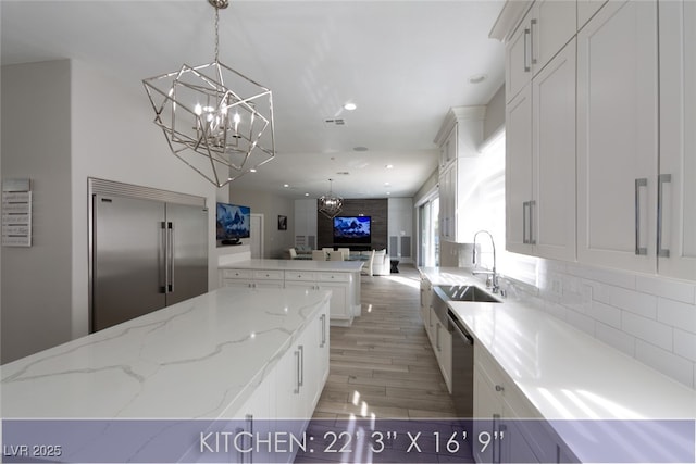 kitchen with open floor plan, an inviting chandelier, stainless steel appliances, white cabinetry, and a sink