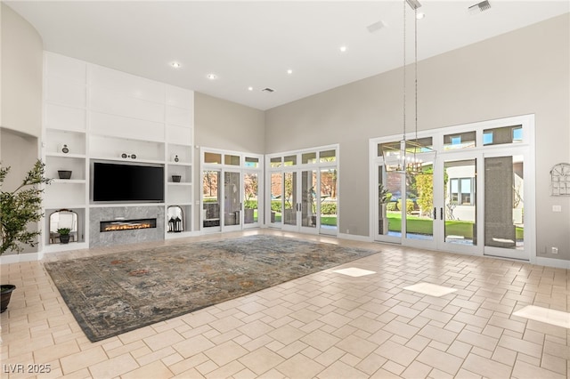 unfurnished living room with built in shelves, a notable chandelier, a premium fireplace, a towering ceiling, and french doors