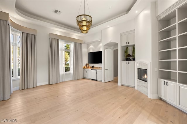 unfurnished living room featuring light wood-style floors, a tray ceiling, visible vents, and a fireplace