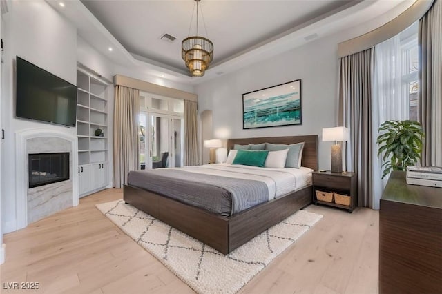 bedroom with a high end fireplace, a raised ceiling, visible vents, and wood finished floors