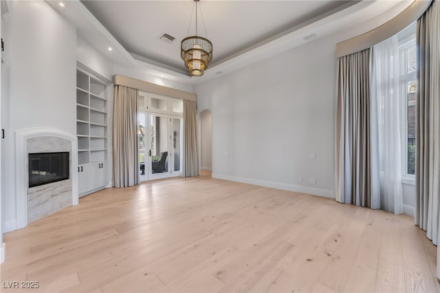 unfurnished living room with a tray ceiling, visible vents, a premium fireplace, and wood finished floors