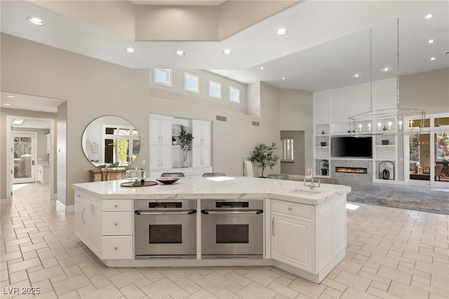 kitchen with a high ceiling, a warm lit fireplace, white cabinetry, and open floor plan