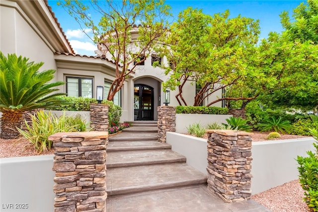 view of exterior entry featuring stucco siding, a tiled roof, and french doors