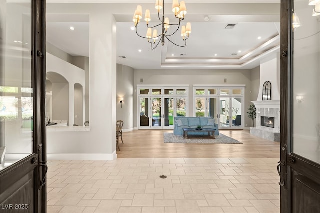 entrance foyer with french doors, a raised ceiling, visible vents, a premium fireplace, and baseboards