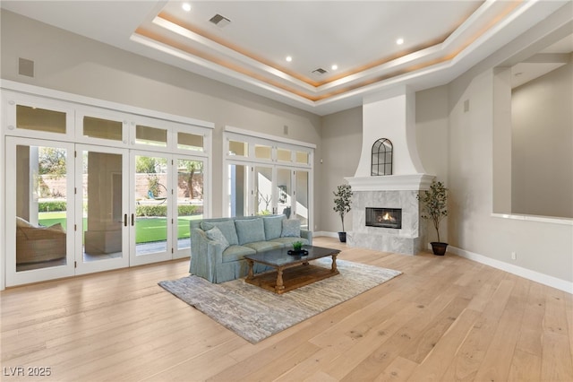 living room featuring a tray ceiling, french doors, wood-type flooring, visible vents, and a high end fireplace