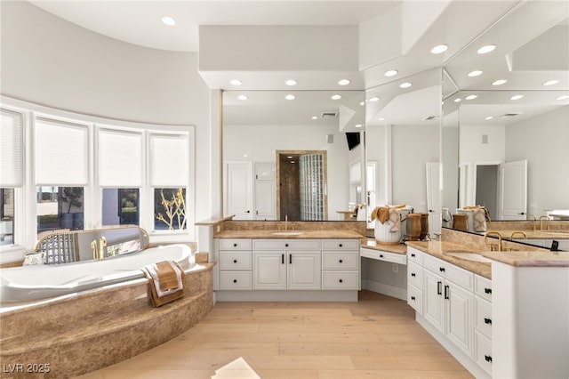 bathroom with recessed lighting, vanity, a bath, and wood finished floors