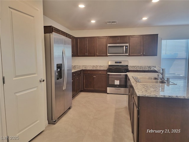 kitchen with a sink, visible vents, dark brown cabinets, appliances with stainless steel finishes, and light stone countertops