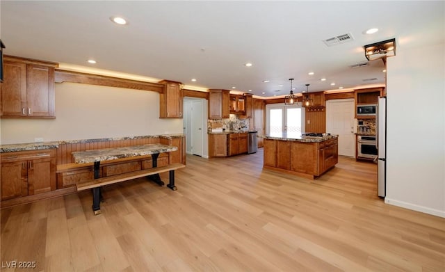 kitchen featuring a kitchen island, visible vents, appliances with stainless steel finishes, brown cabinetry, and decorative light fixtures