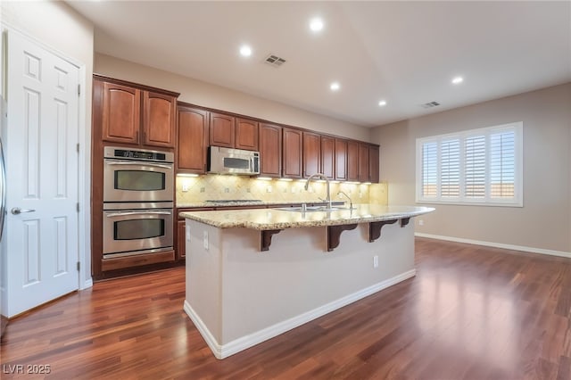 kitchen with light stone counters, a breakfast bar, a sink, visible vents, and appliances with stainless steel finishes