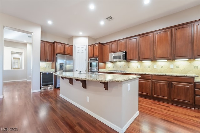 kitchen featuring a breakfast bar area, stainless steel appliances, visible vents, dark wood-type flooring, and light stone countertops