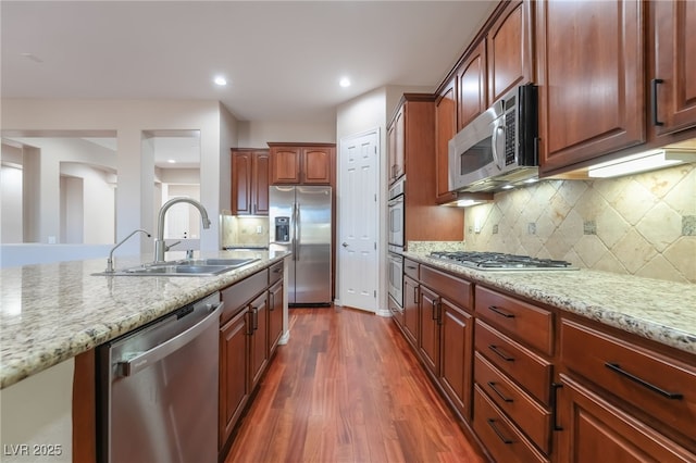 kitchen featuring dark wood-style floors, stainless steel appliances, backsplash, a sink, and light stone countertops