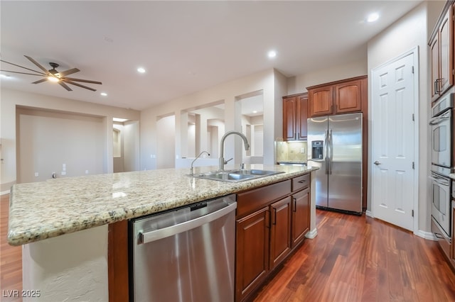 kitchen featuring a center island with sink, dark wood finished floors, appliances with stainless steel finishes, light stone countertops, and a sink