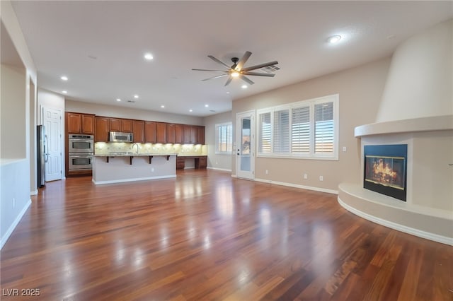 unfurnished living room with recessed lighting, dark wood-type flooring, a large fireplace, a sink, and baseboards