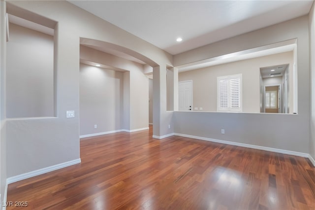 spare room featuring baseboards, arched walkways, wood finished floors, and recessed lighting