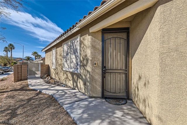 entrance to property featuring a gate, a tiled roof, and stucco siding