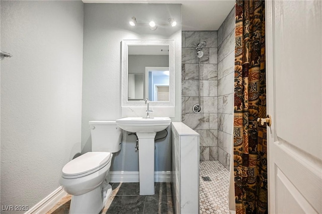 bathroom featuring toilet, baseboards, walk in shower, and a sink