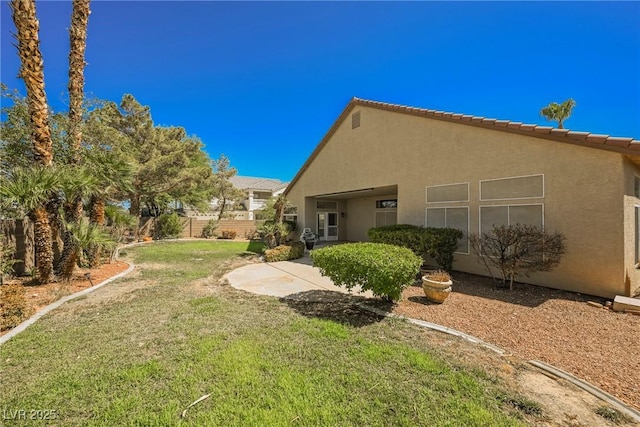 rear view of property featuring a yard, a patio, fence, and stucco siding