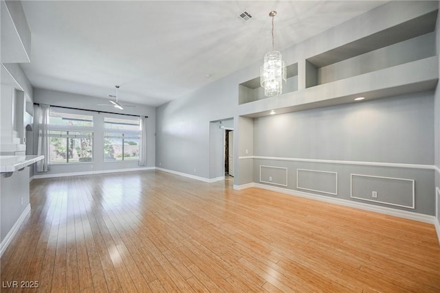 unfurnished living room featuring visible vents, light wood-style flooring, baseboards, and ceiling fan with notable chandelier