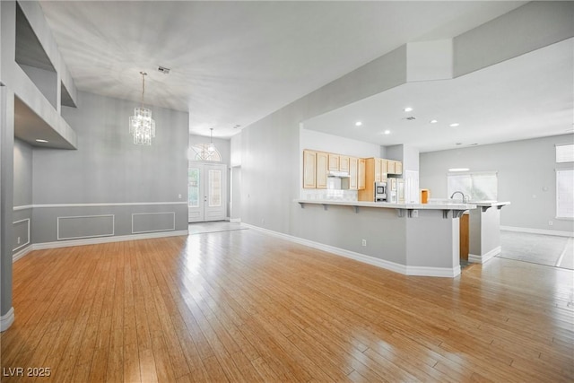 unfurnished living room with a chandelier, recessed lighting, a sink, baseboards, and light wood finished floors