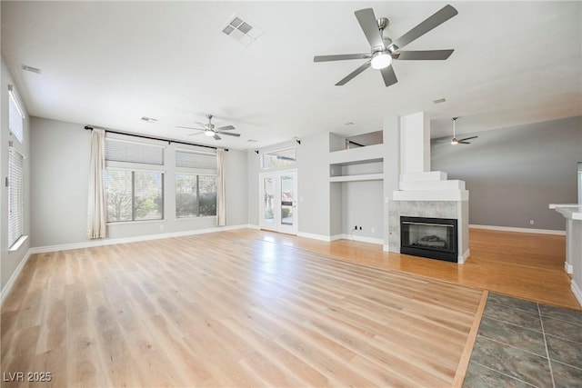 unfurnished living room with a ceiling fan, visible vents, baseboards, light wood finished floors, and a tiled fireplace