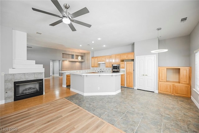 kitchen with a kitchen island, open floor plan, light countertops, stainless steel microwave, and pendant lighting