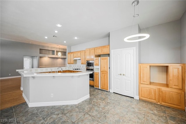 kitchen with pendant lighting, light countertops, an island with sink, and built in appliances