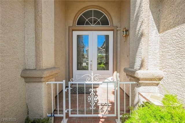 doorway to property featuring stucco siding, a gate, and french doors