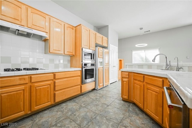 kitchen with tile countertops, decorative backsplash, appliances with stainless steel finishes, a sink, and under cabinet range hood