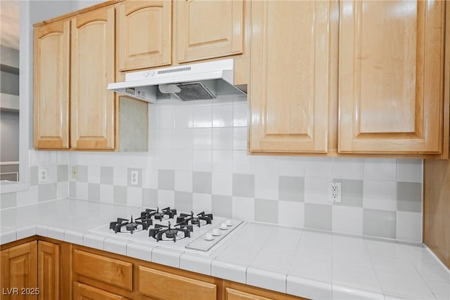 kitchen featuring tile countertops, under cabinet range hood, white gas stovetop, and backsplash