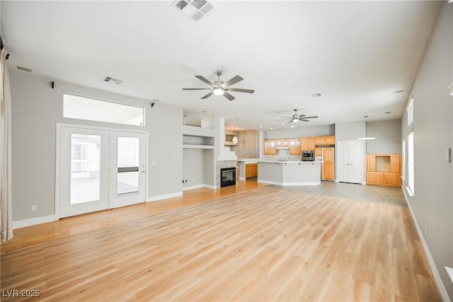 unfurnished living room featuring a glass covered fireplace, visible vents, ceiling fan, and light wood-style flooring