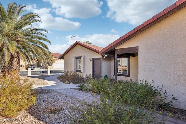 view of side of property with a tile roof, fence, and stucco siding