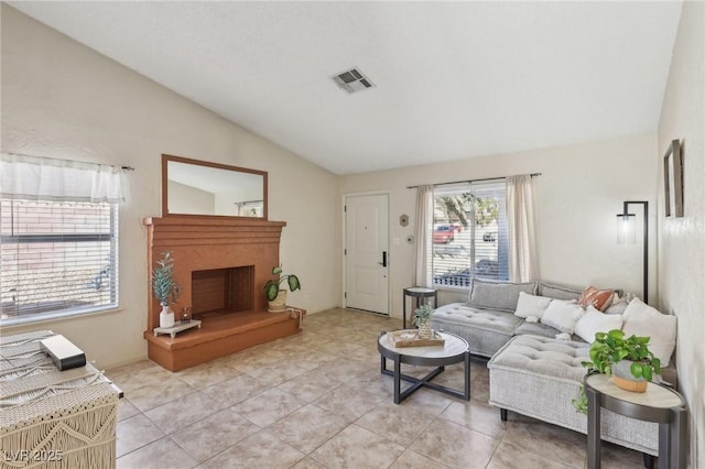 living area with a fireplace with raised hearth, light tile patterned floors, visible vents, and vaulted ceiling