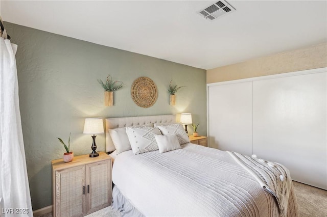 bedroom with a textured wall, visible vents, a closet, and light colored carpet