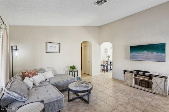 living area with light tile patterned floors, visible vents, arched walkways, vaulted ceiling, and a textured ceiling