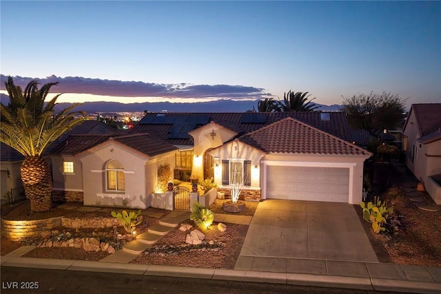 mediterranean / spanish house with a garage, driveway, solar panels, a tiled roof, and stucco siding