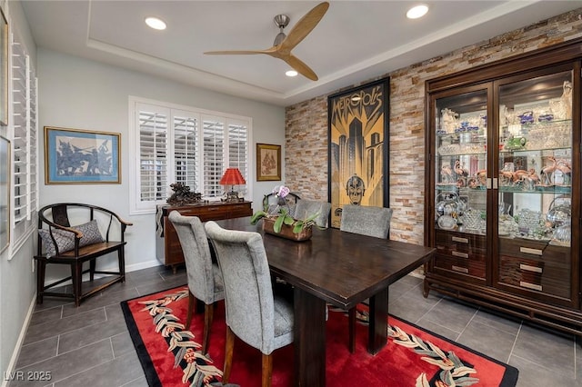 dining space with dark tile patterned floors, a raised ceiling, a ceiling fan, and baseboards