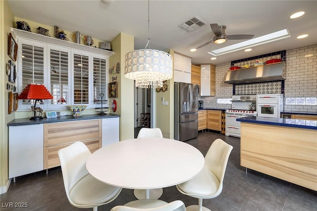 kitchen featuring range with two ovens, visible vents, stainless steel fridge with ice dispenser, light brown cabinetry, and dark countertops