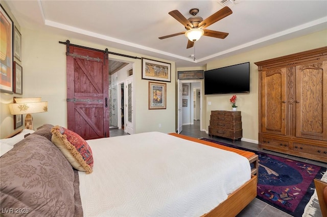 bedroom featuring visible vents, a tray ceiling, a barn door, and a ceiling fan