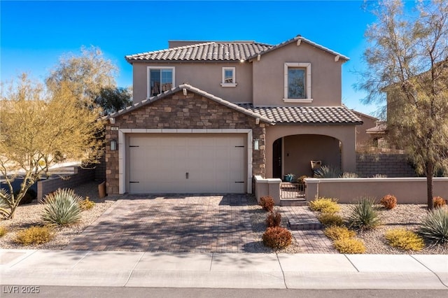 mediterranean / spanish-style home featuring stone siding, decorative driveway, a tiled roof, and stucco siding