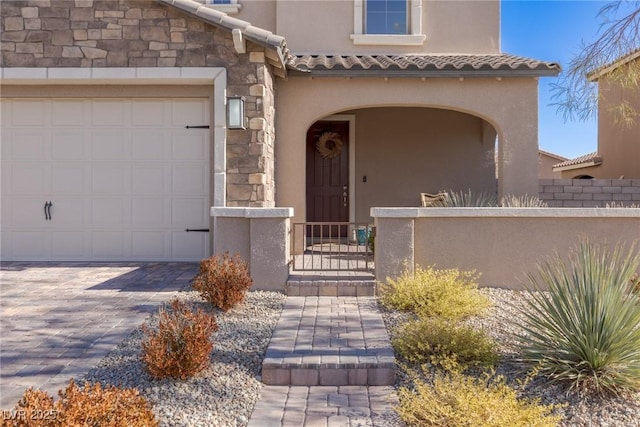 entrance to property featuring stone siding, a tile roof, an attached garage, and stucco siding