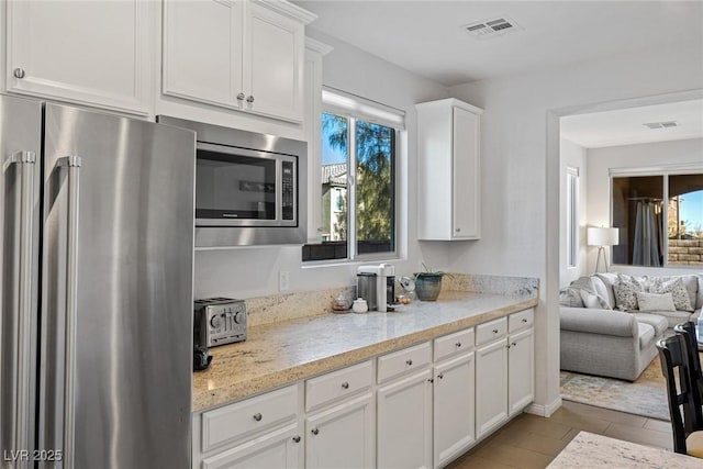 kitchen featuring light stone counters, stainless steel appliances, visible vents, open floor plan, and white cabinetry