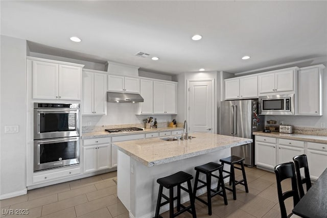 kitchen featuring under cabinet range hood, stainless steel appliances, a breakfast bar, a sink, and a center island with sink