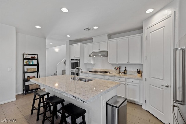 kitchen with a kitchen island with sink, white cabinets, a sink, and under cabinet range hood