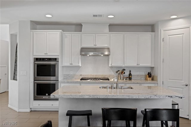 kitchen featuring under cabinet range hood, stainless steel appliances, a sink, visible vents, and white cabinets