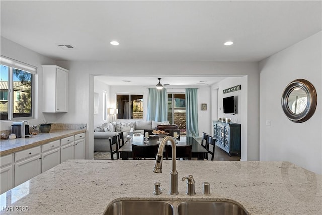 kitchen featuring light stone counters, a sink, visible vents, white cabinets, and open floor plan