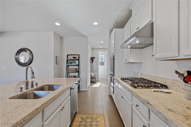 kitchen with white cabinets, appliances with stainless steel finishes, light stone countertops, under cabinet range hood, and a sink