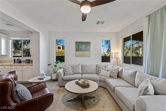 living room featuring a ceiling fan, visible vents, and a wealth of natural light