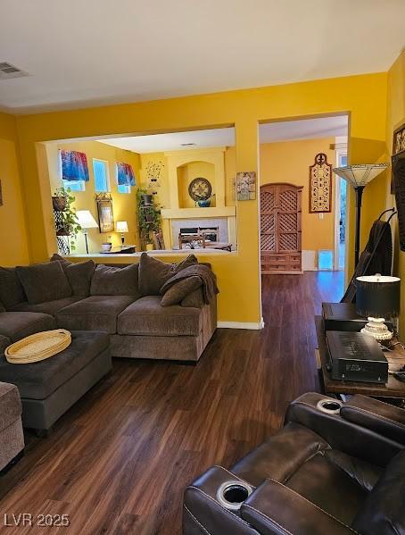 living area featuring baseboards, a fireplace, visible vents, and dark wood-style flooring