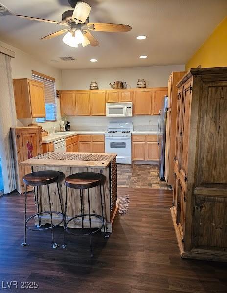 kitchen with light brown cabinetry, white appliances, dark wood finished floors, and visible vents